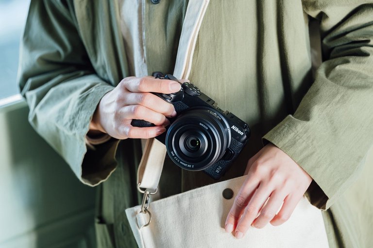 Hands holding the Nikon Z DX 24mm f/1.7 lens on a Nikon Z30 camera body