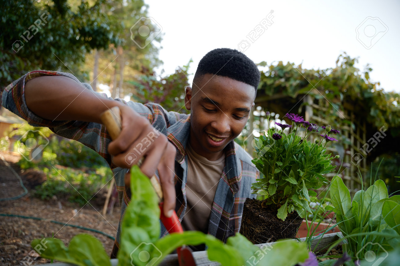 197004690-feliz-joven-negro-sonriendo-mientras-usa-una-pala-en-un-huerto-en-el-centro-del-jardín.jpg