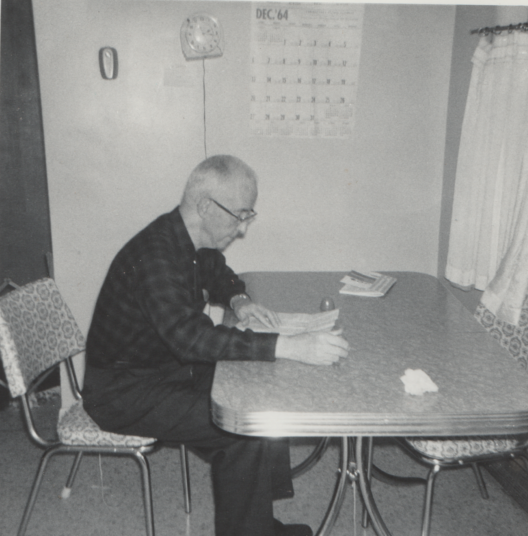 1964-12 - Charles Dwight Pickett, sitting on a chair at a kitchen table or something in black and white, calendar says Dec 64 but was developed in Feb 1965, 1pic.png