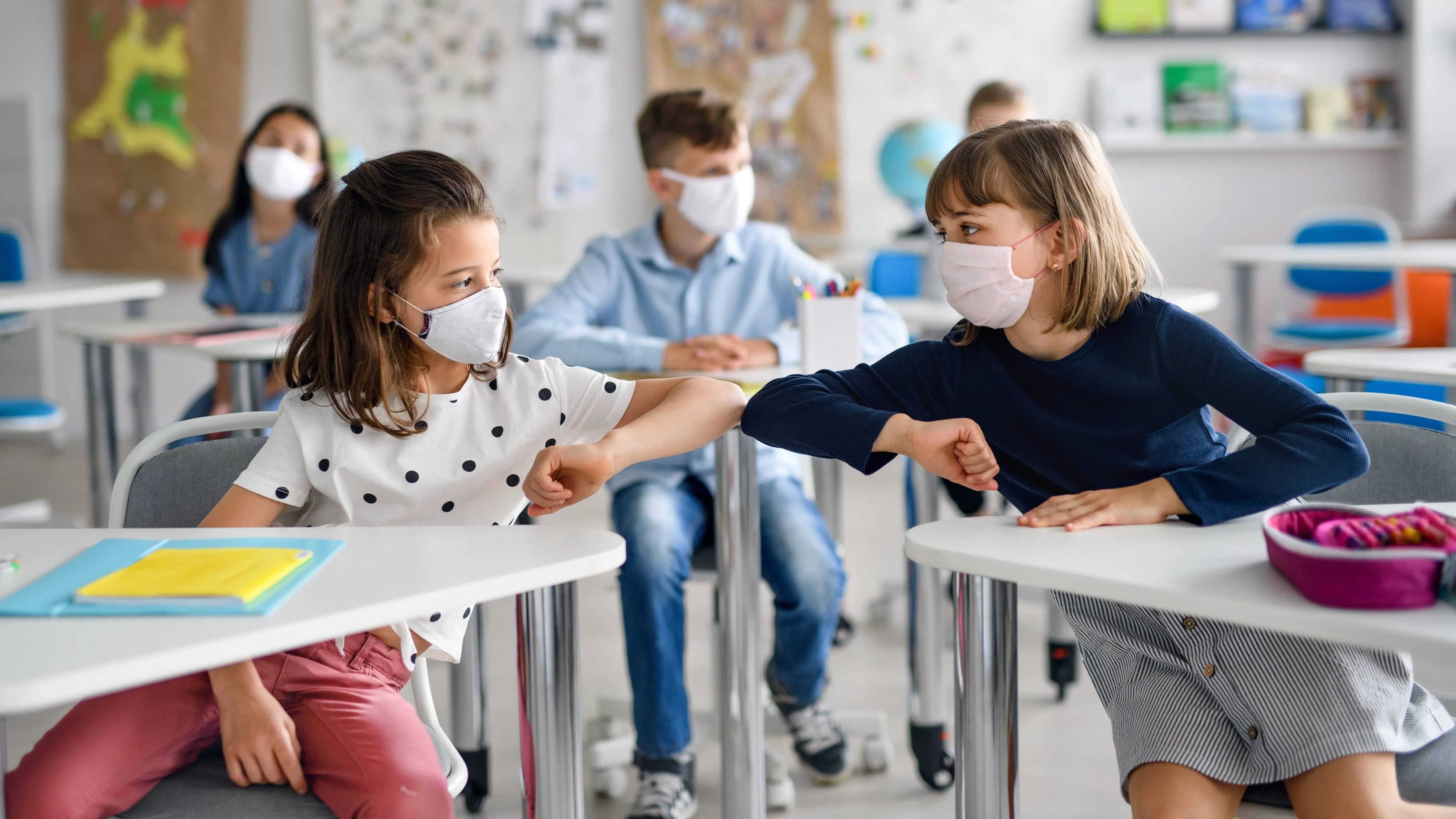 a-classroom-of-elementary-or-middle-school-aged-children-wearing-masks-and-praticing-social-distancing-touching-elbows-16x9-1.webp