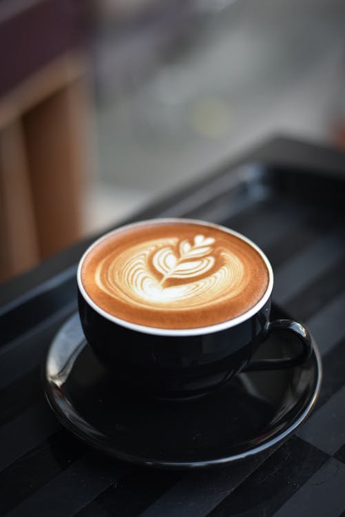 Free A beautifully crafted cappuccino with intricate latte art in a black ceramic mug on a dark surface. Stock Photo